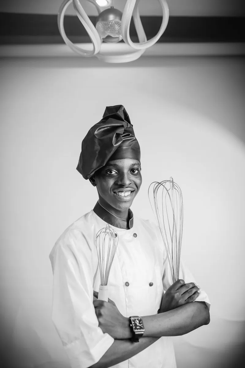 Smiling chef in uniform holding whisks, showcasing culinary expertise and confidence.