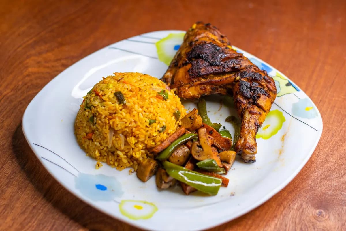Delicious grilled chicken served with flavorful Jollof rice and sautéed vegetables on a white plate.
